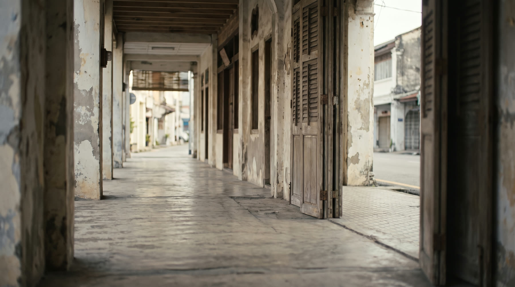 The five-foot way of an old Malaysian shophouse in morning light, with patterned floor tiles and a turquoise shutter door.